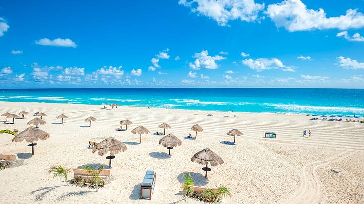 Aerial of blue water and a stunning white sandy beach with nipa hut umbrellas