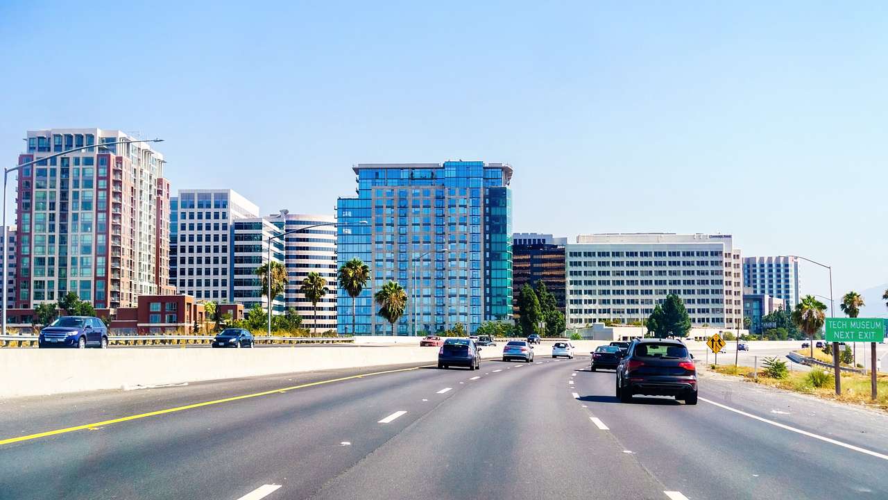 Cars driving along a highway with a cityscape full of buildings and blue sky behind