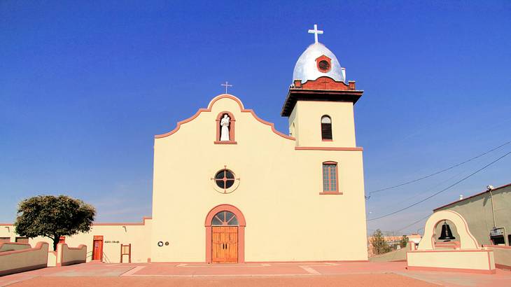 A small yellow church with a bell tower and a cross at the top, on a clear blue day