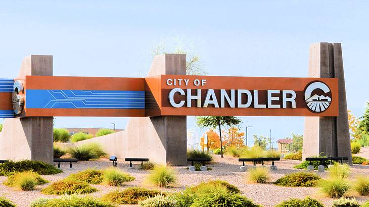 An orange and white concrete road sign titled City of Chandler with dessert around