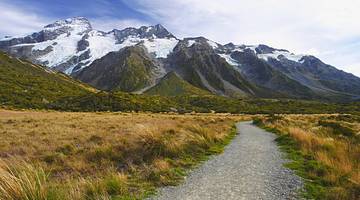 Snow-capped mountains at the back with a gravel path and grassy field in front
