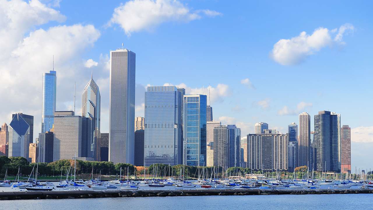 A lake filled with boats with an urban skyline in the background on a nice day