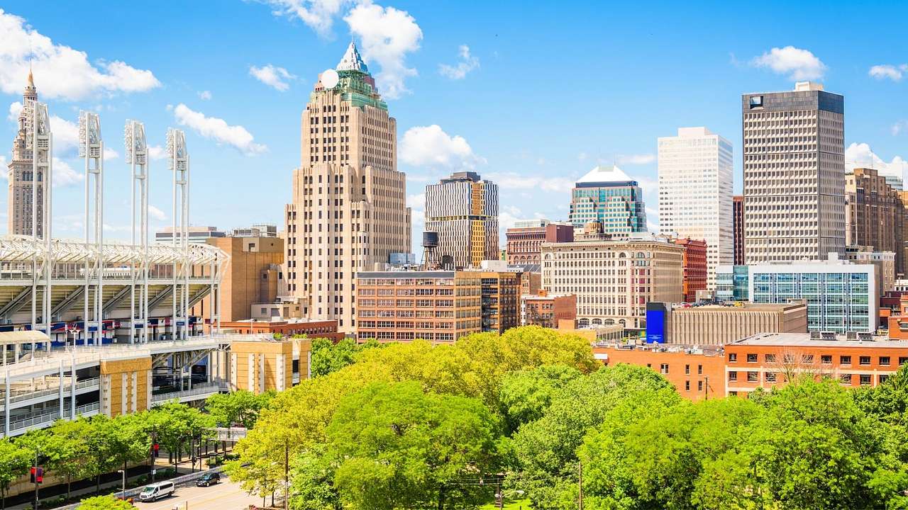A city skyline with greenery in front of it, under a blue sky with some clouds