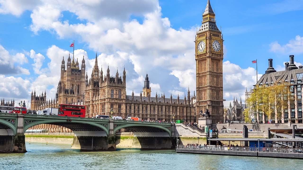 A tall clock tower with a large rectangular building and a bridge on the left