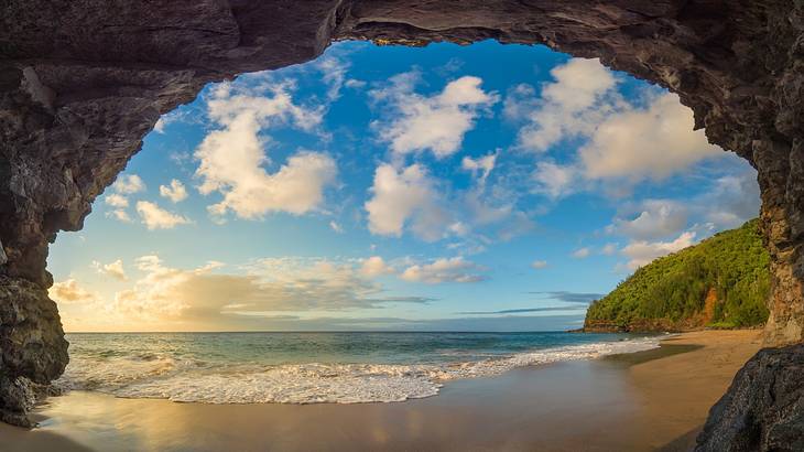 View of a beautiful sandy beach under a partly cloudy sky through a cave