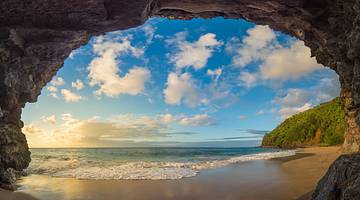 View of a beautiful sandy beach under a partly cloudy sky through a cave