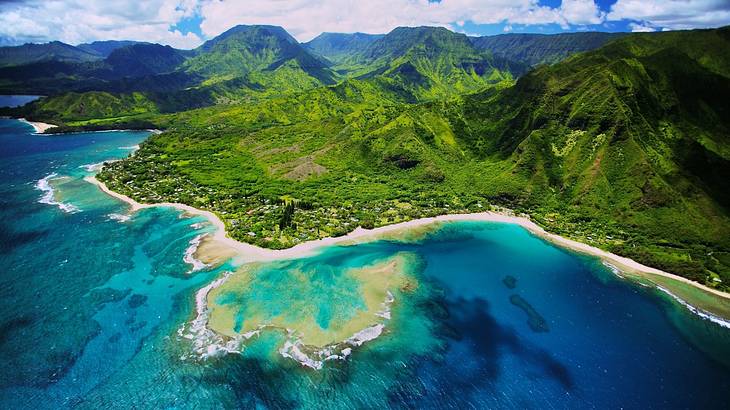 Top view of sandy coastline where green mountains meet deep blue ocean waters