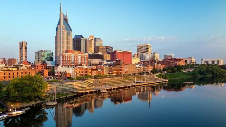 A city skyline with a river and trees in front of it under a blue sky