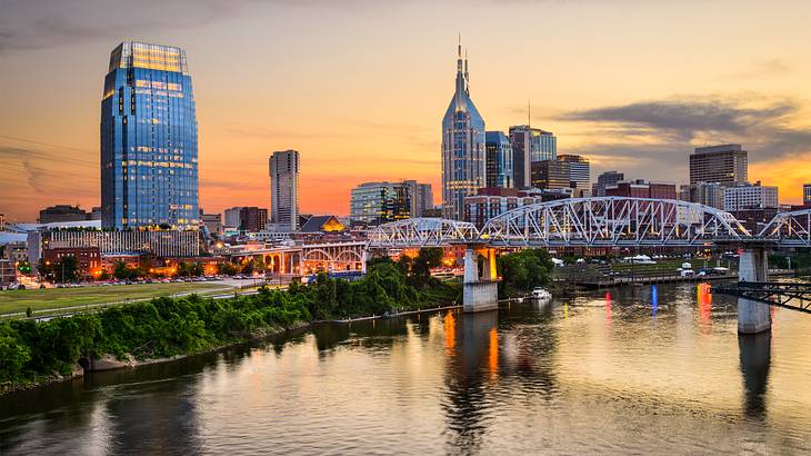 A city skyline with tall buildings at sunset and a bridge over water in front