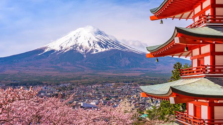 A snow-capped mountain peak with a red pagoda on the right and pink blossom trees