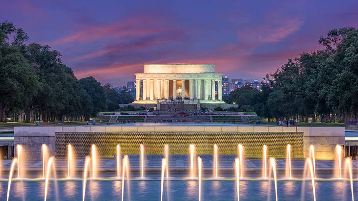 Water fountains in front of a stone building with trees surrounding it at night