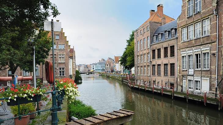 A channel in the centre of old buildings with a dock and greenery on the left