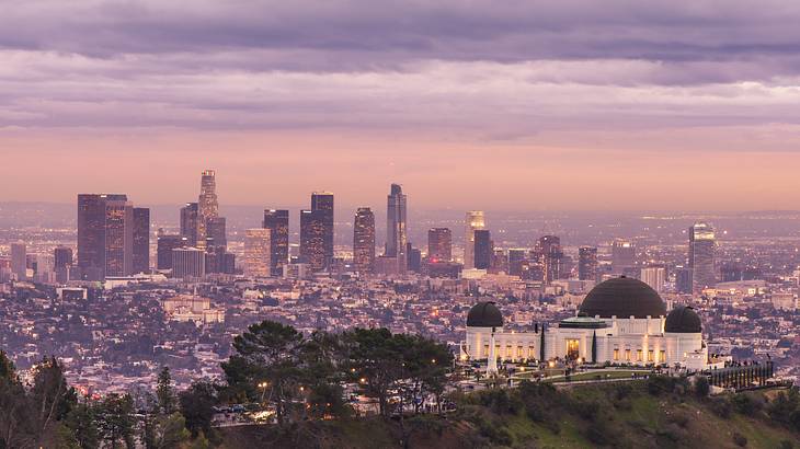 A park and observatory on top of a mountain with a pink cityscape in the background