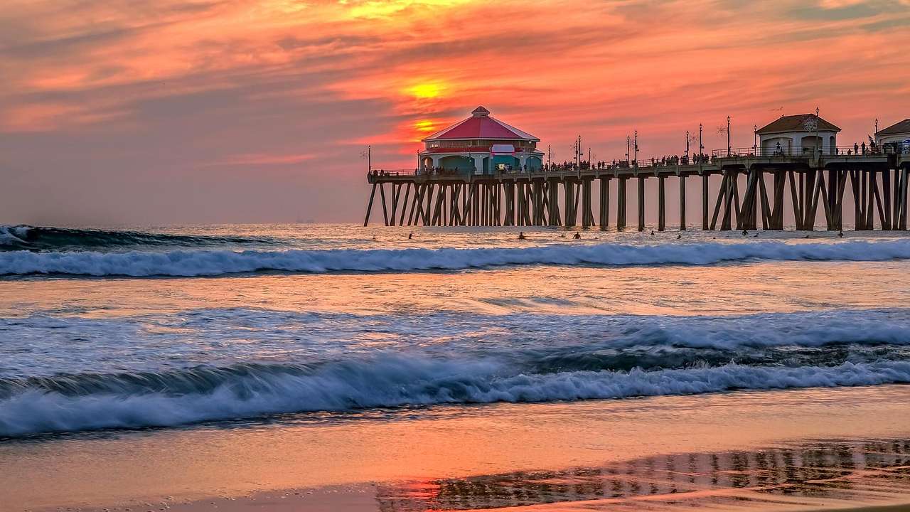 Ocean waves beneath a wooden pier with a conical-shaped hut at sunset