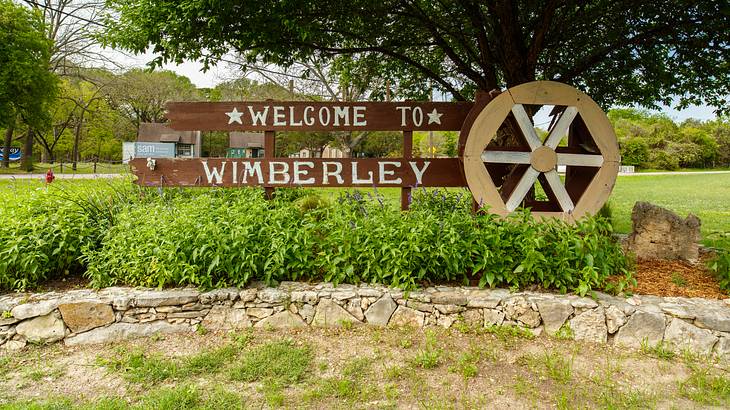 A "welcome to Wimberley" sign with a wheel on the right, surrounded by greenery