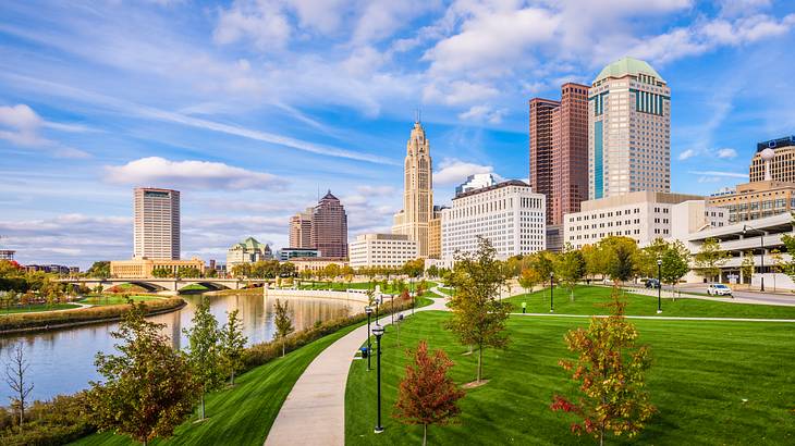 An urban park beside a river with a city skyline in the background