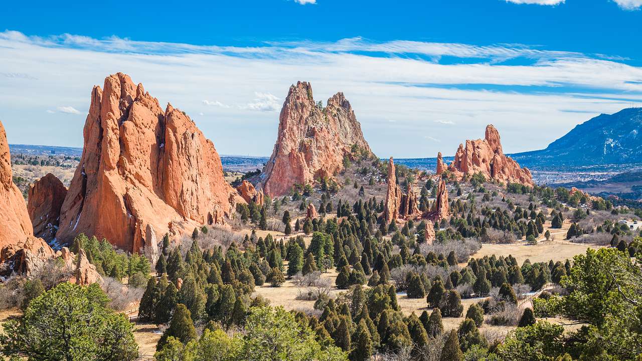 Several tall & massive red rocks surrounded by green trees under a partly cloudy sky