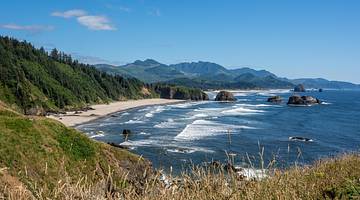 A view across a beach, with a sandy shore, the ocean, and greenery-covered hills