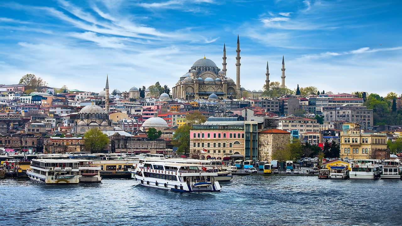 A huge mosque surrounded by colorful buildings overlooking water with cruise boats
