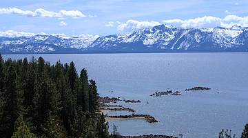 A snow-capped mountain range behind a lake with evergreen trees to the left