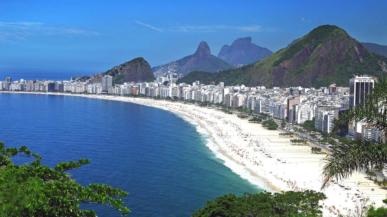Side view of lush green mountains along a white sand beach lined with buildings