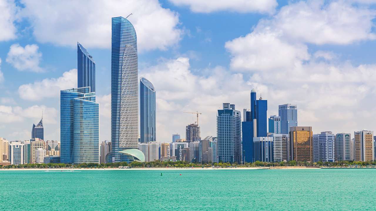 A skyline with tall glass buildings against a partly cloudy sky overlooking the water
