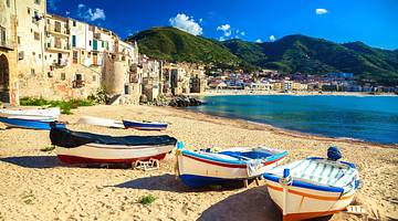 Boats sitting on the sand next to ocean water with mountains and a town to the side