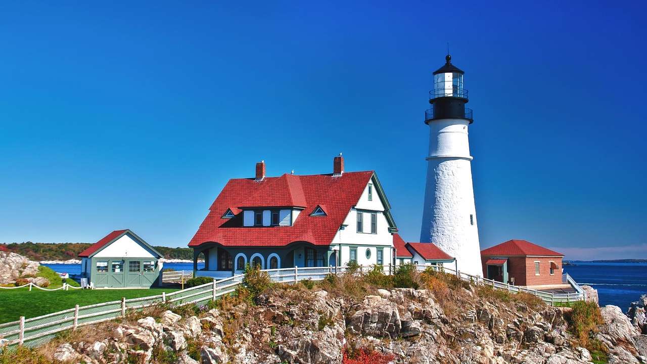 A white and black lighthouse next to a house with a red roof on a cliff by the ocean
