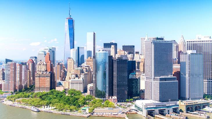 The Manhattan skyline with highrise buildings behind greenery and a harbor