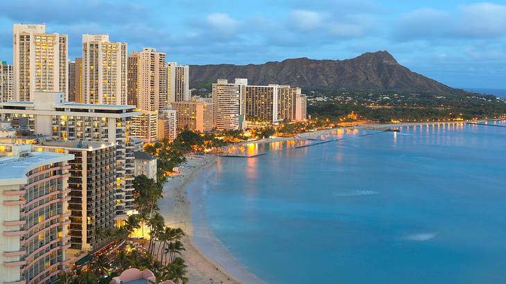 A beach with illuminated buildings and a mountain to the side at night