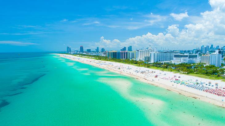 Aerial shot of buildings and greenery along a white sand beach on a nice day Aerial shot of buildings and greenery along a white sand beach on a nice day