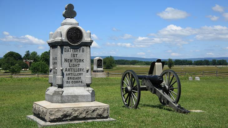 A granite monument and an old black canon on a grassy field with trees in the back