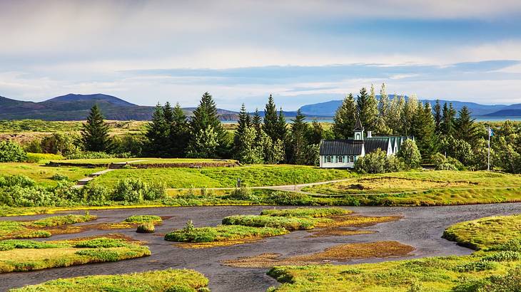 A small building surrounded by grass with alpine trees and mountains behind it