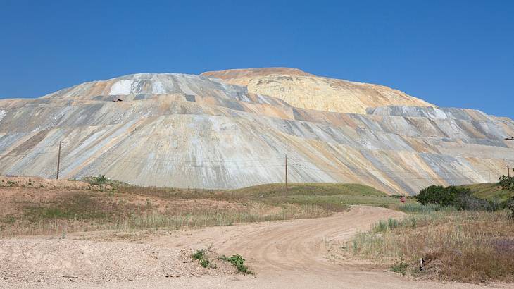 A hill at a mining site with a sandy path in front of it under a blue sky