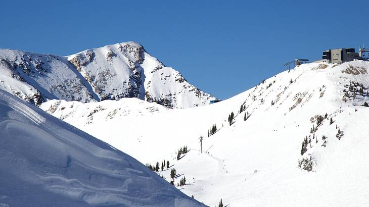 Snow-covered hills with some trees and a small building under a blue sky Snow-covered hills with some trees and a small building under a blue sky