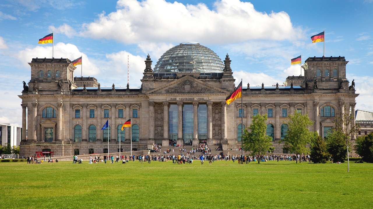 A large stone building with a glass dome roof and German flags near grass