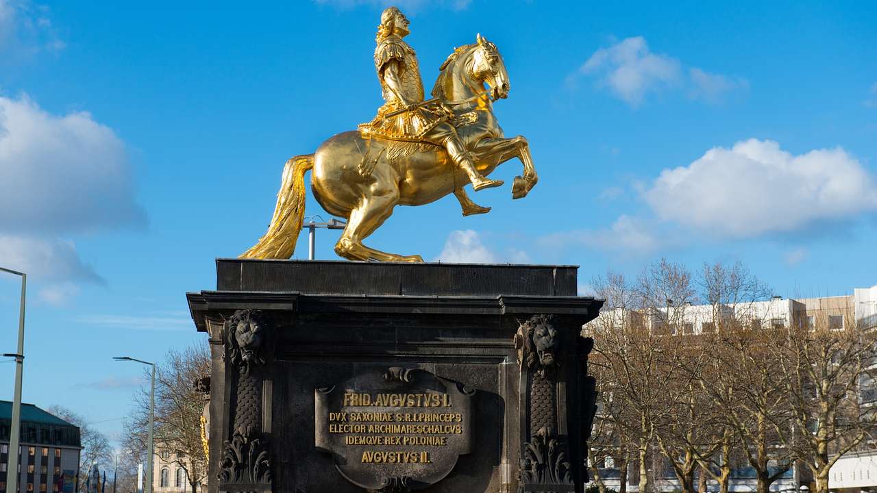 A golden statue of a man in armor on a horse on top of a black podium with a plaque