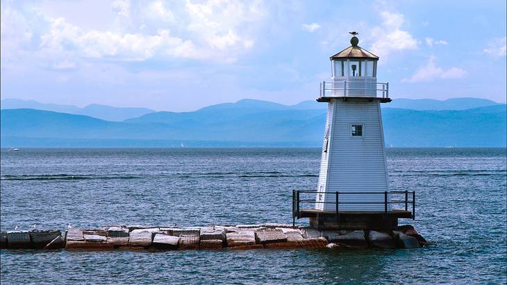 A small white lighthouse on a lake with hills in the distance A small white lighthouse on a lake with hills in the distance