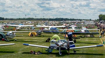 Many light planes parked on a grassy field for an event