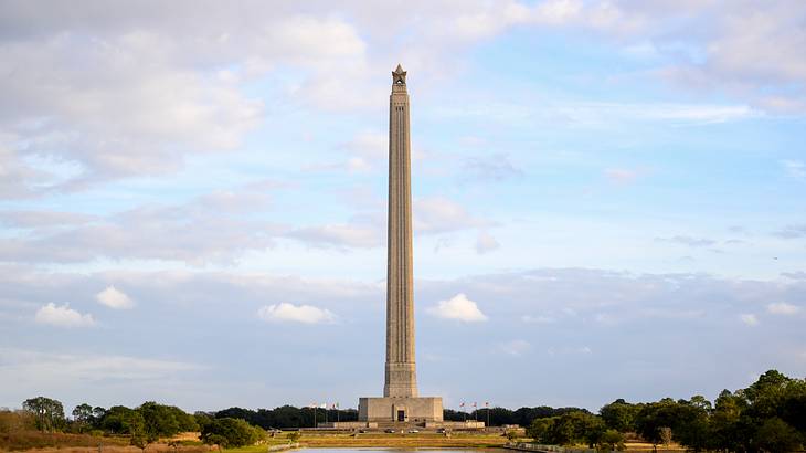 A tall monument with a body of water in front and greenery in the background