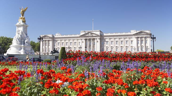 A white palace with a statue on the left, and red and purple flowers in front