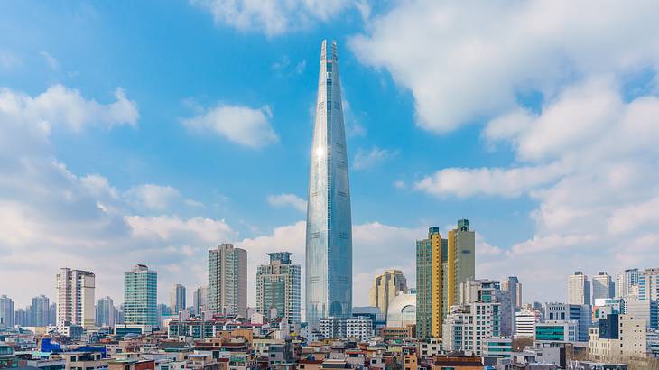 A modern glass tower next to other city buildings under a blue sky with clouds