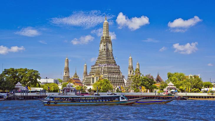 A temple structure with five towers next to trees and a river with a boat on it