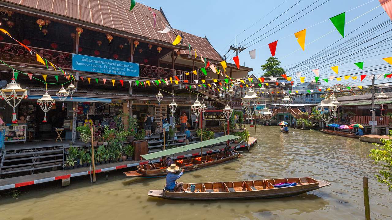 A longtail boat on a river next to a building with colourful flags above