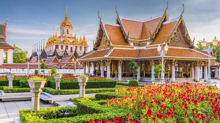 A temple with gold details next to another ornate building and a garden