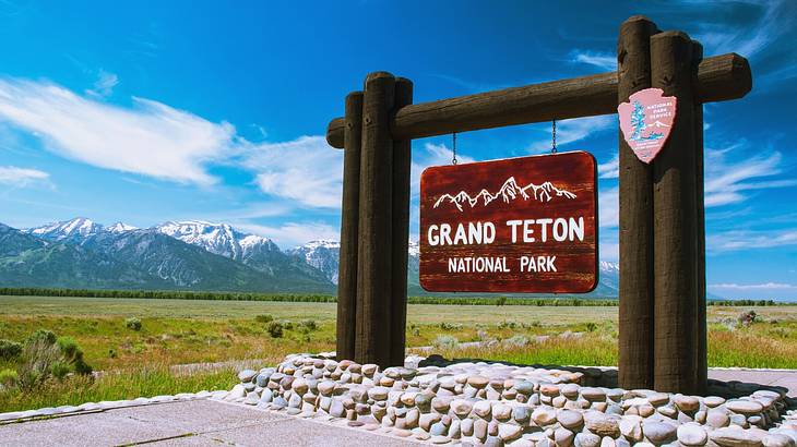 A wooden sign that says "Grand Teton National Park" next to grass and mountains