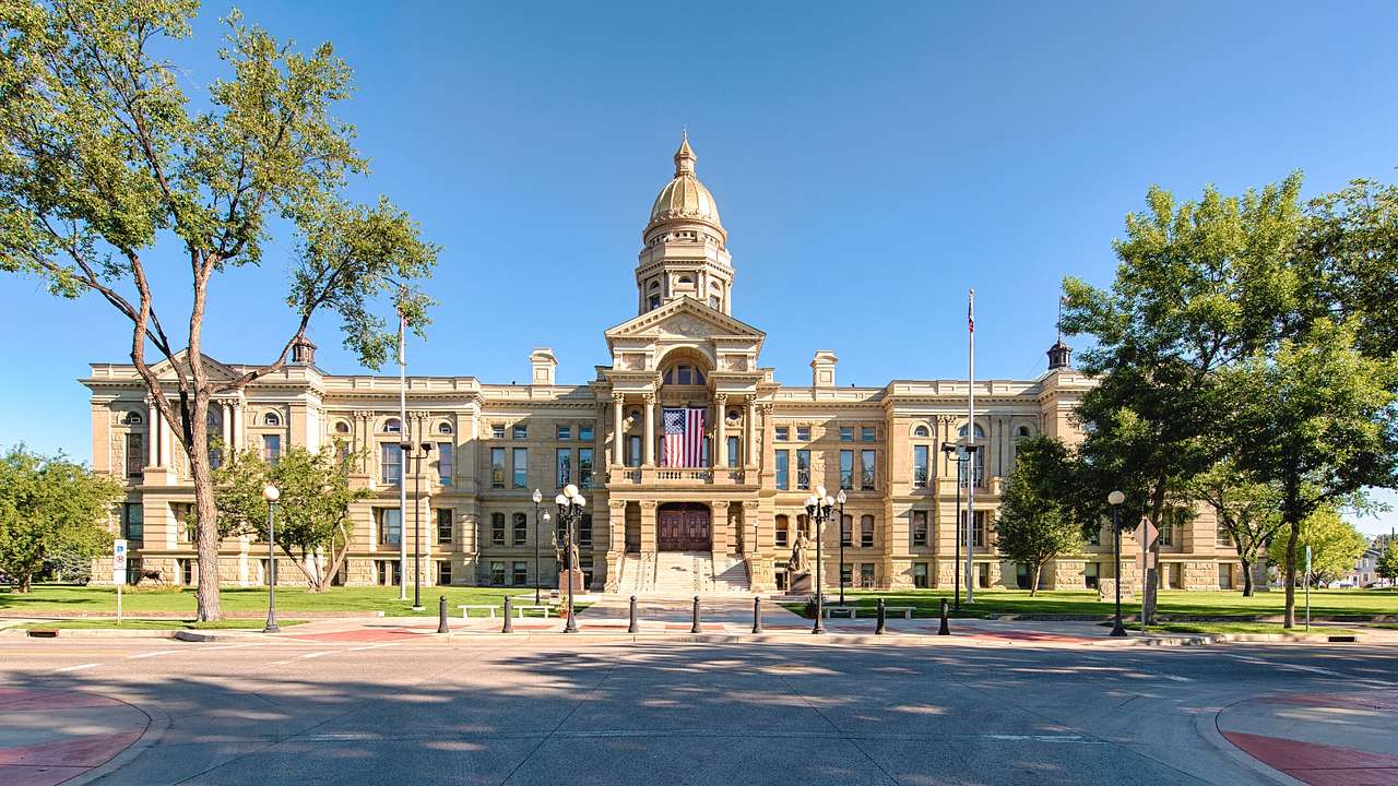 A large state capitol building with a gold dome next to trees and grass