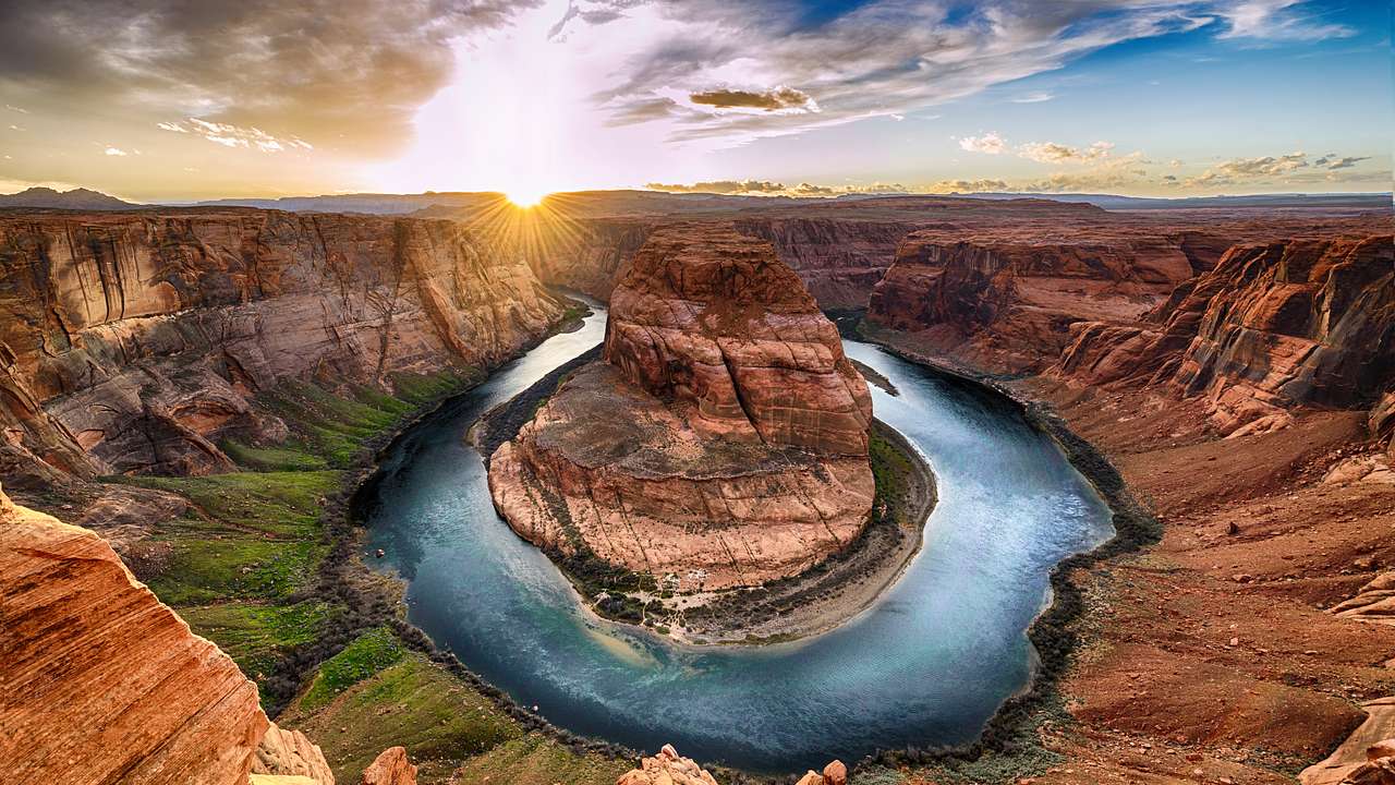 A large rock in a body of water surrounded by a canyon and a sunset in the background