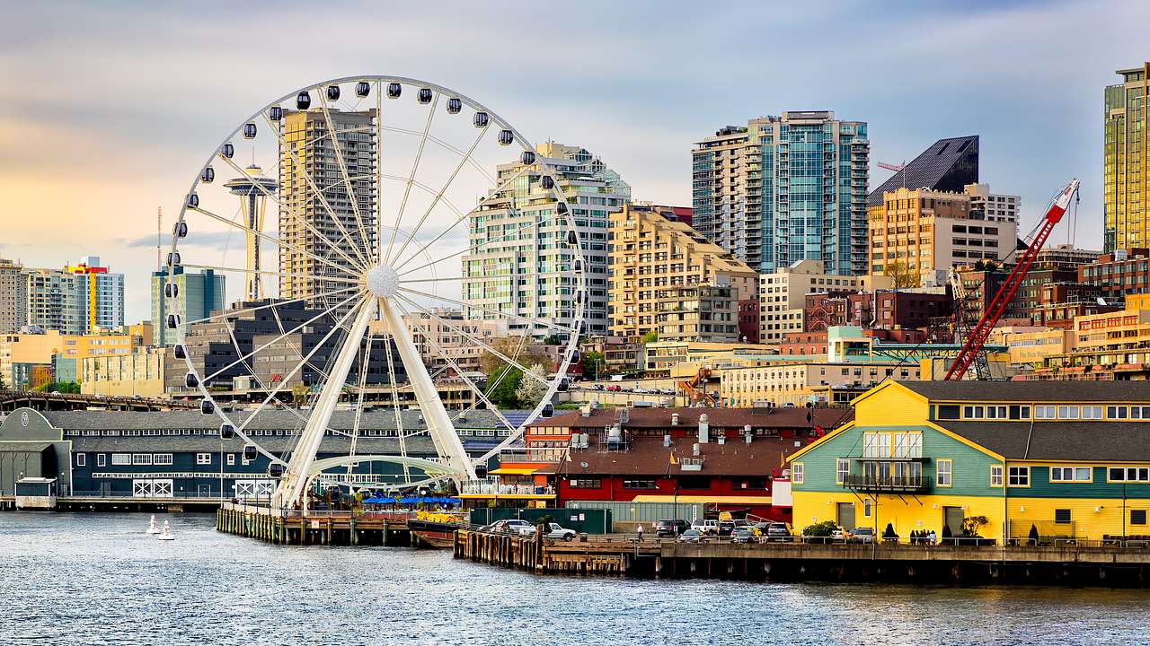 A Ferris wheel by a body of water with buildings in the background