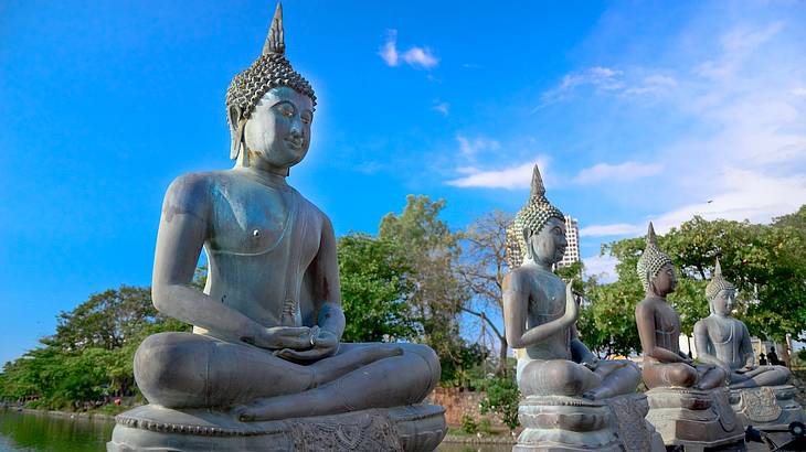 Buddha statues lined up in a row with trees behind at Seema Malaka Temple, Colombo